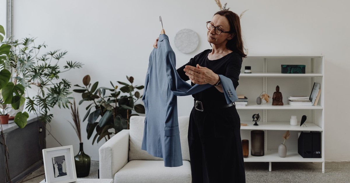 A woman in a modern living room holding a blue suit jacket pensively.