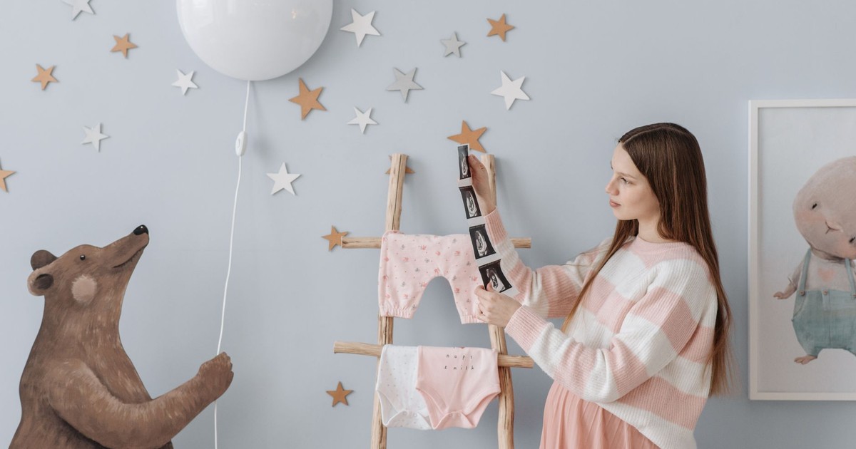 Expectant mother holding ultrasound images in a beautifully decorated nursery with whimsical elements.