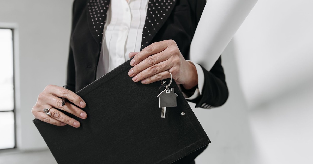 Close-up of a realtor holding a keychain and clipboard with interior office background.