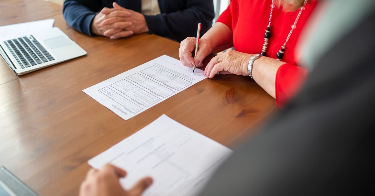 Two adults sign documents on a wooden table at a business meeting, emphasizing teamwork.