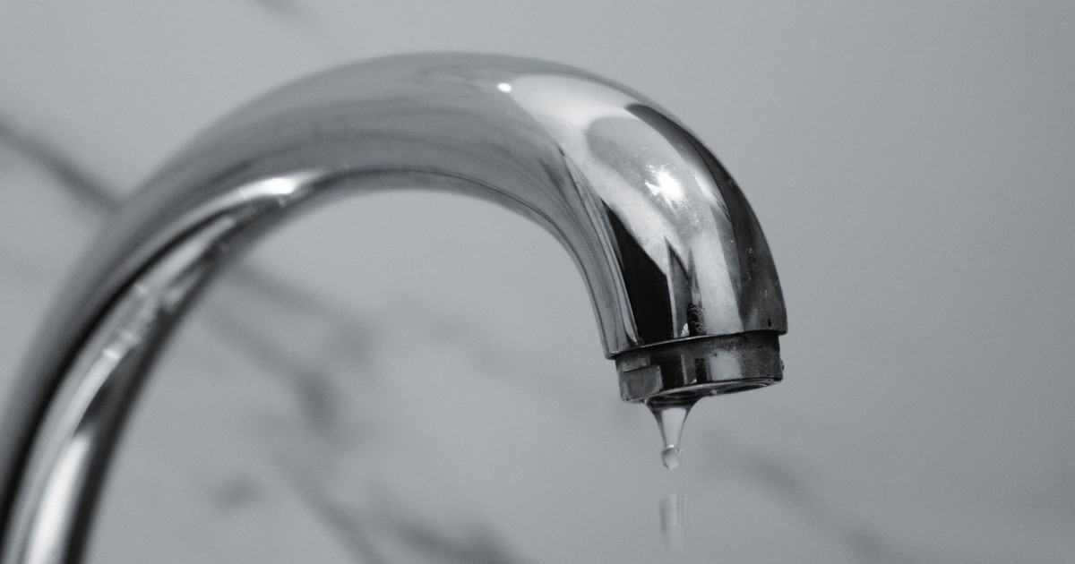 A close-up shot of a modern chrome bathroom faucet with water dripping from the tip.