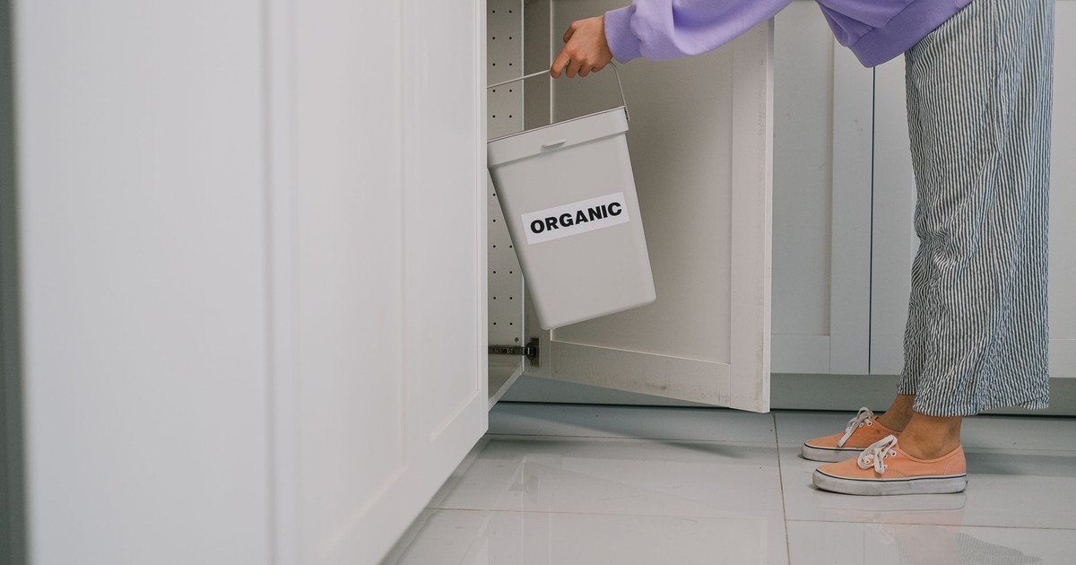 A person placing an organic waste bin inside a modern kitchen cabinet, promoting sustainable living.