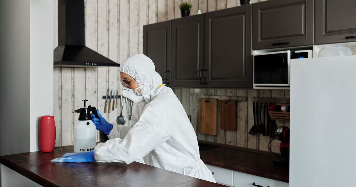 A worker in protective gear disinfects a kitchen, ensuring a clean and safe environment.