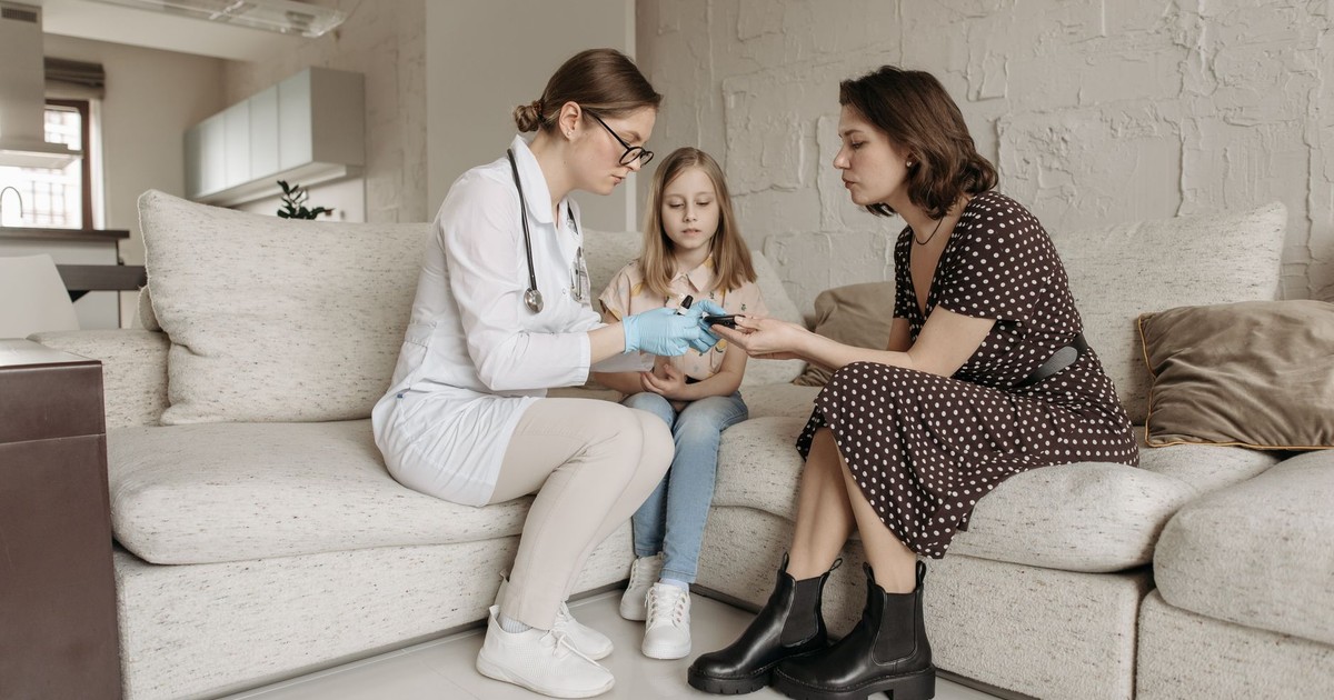 A medical professional examines a child's hand while the mother watches closely.