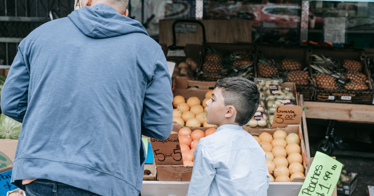 Father and son explore a bustling farmer's market filled with fresh produce.