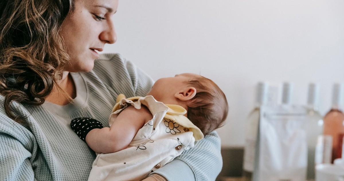Side view of crop caring mother in casual wear with cute newborn baby in arms standing in light room at home