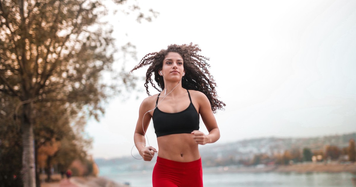 Determined woman in red leggings jogging along a scenic riverside path, embracing fitness outdoors.