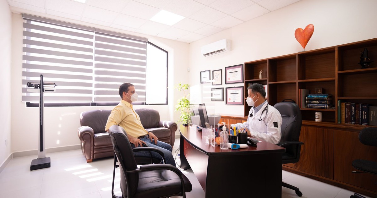 A patient consults with a masked doctor in a well-lit, modern office. Safety measures in place.