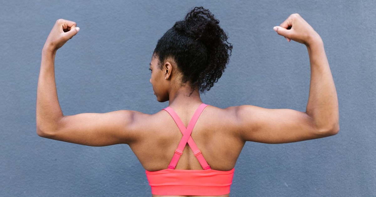 Rear view of a fit woman flexing muscles in a pink sports bra against a gray background.
