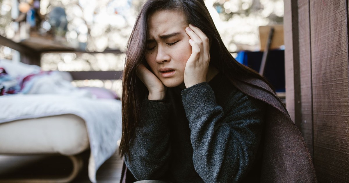 A young woman holds her head in distress while sitting indoors, capturing an emotional moment.