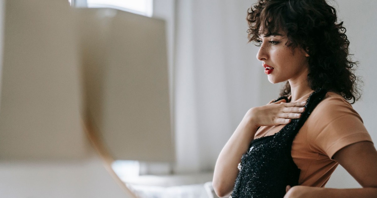 Side view of wistful adult female with black apparel reflecting in mirror and looking away in house