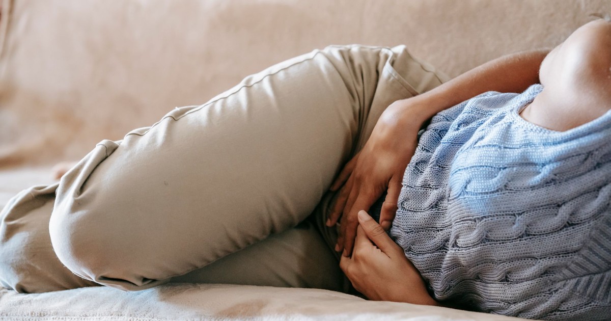 Crop faceless female in casual wear lying on sofa while having acute pain in stomach
