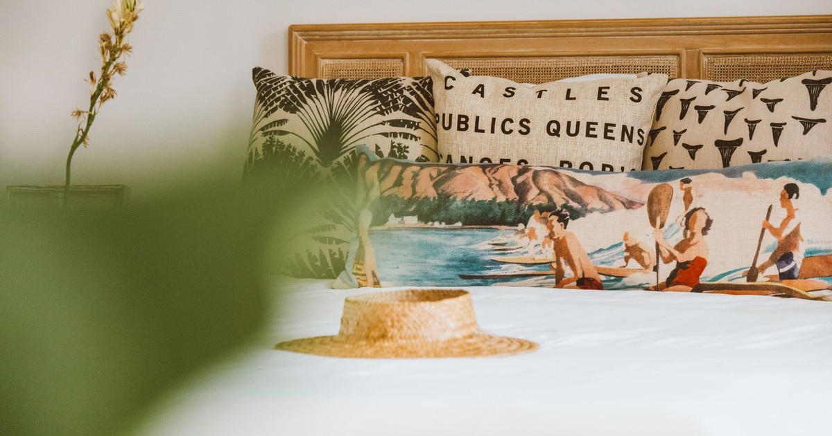 A stylish bed with artistic pillows and a straw hat exuding a relaxed, summer vibe.