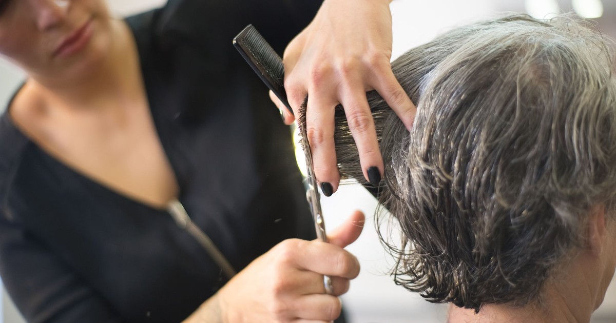 Hairdresser cutting senior woman's hair in a salon with close-up view of the hands and tools.