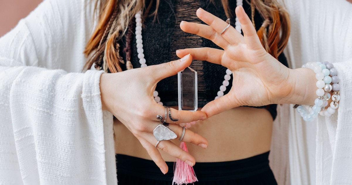 A woman wearing jewelry holds a clear healing crystal, symbolizing spiritual wellness.
