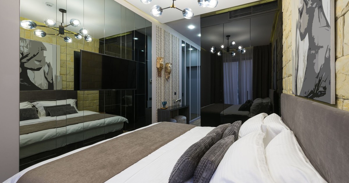 Soft bed with pillows between painting and wall reflecting shiny lights in contemporary hotel bedroom