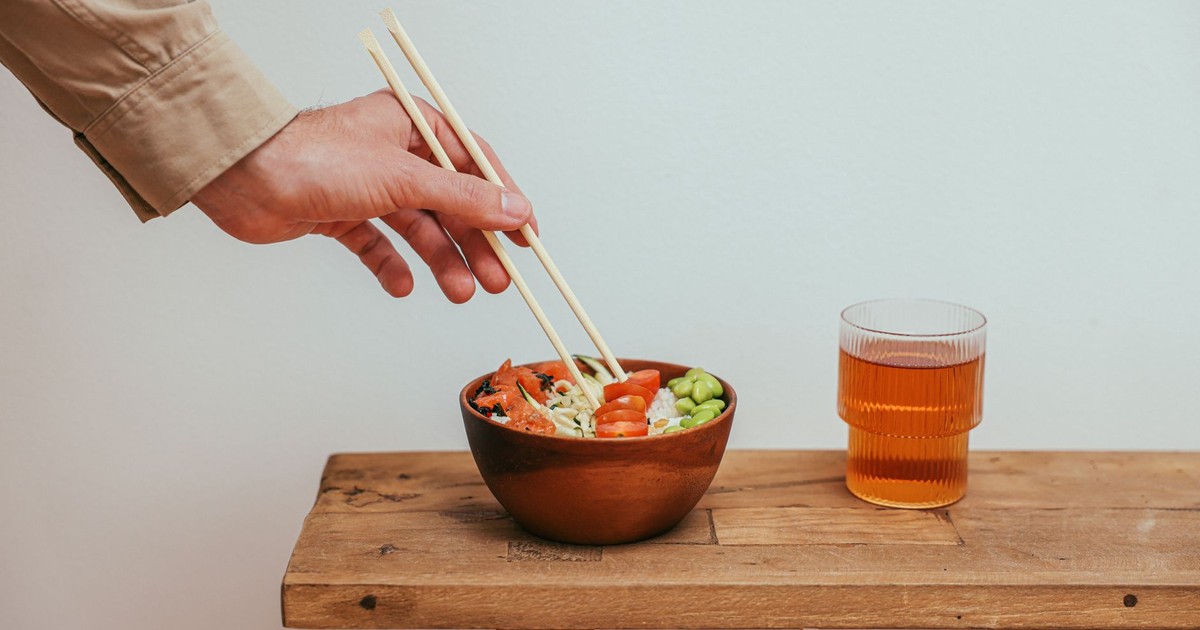 Hand reaching for a colorful rice bowl with edamame and cherry tomatoes with tea.