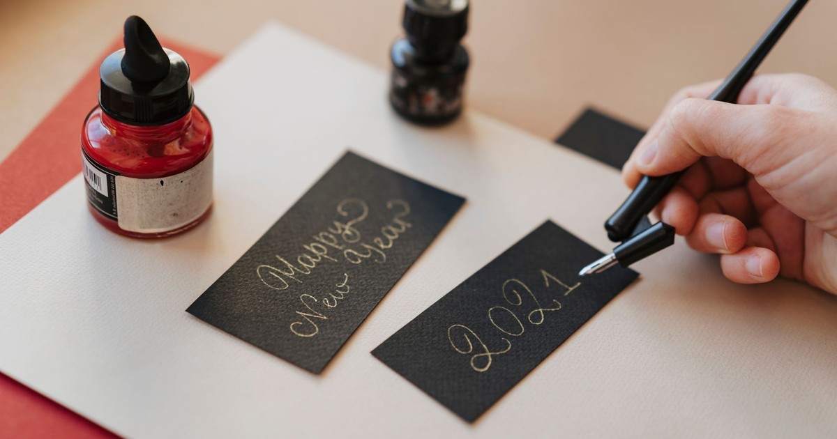 A hand writes 'Happy New Year 2021' in calligraphy with a fountain pen.