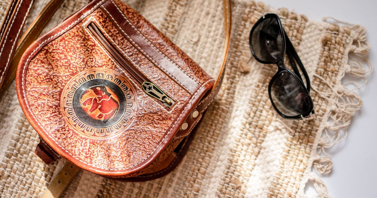 Close-up of a leather handbag and sunglasses on a woven rug with textured pattern.