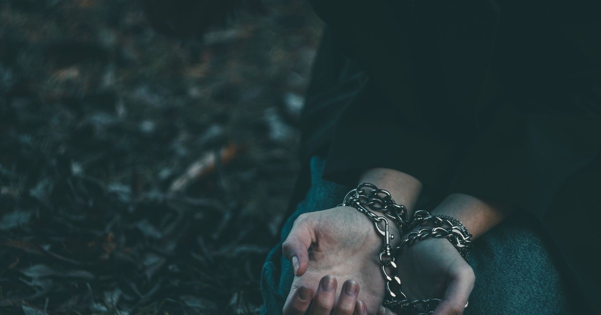 Close-up of a person's hands bound with chains in an outdoor setting, symbolizing confinement.