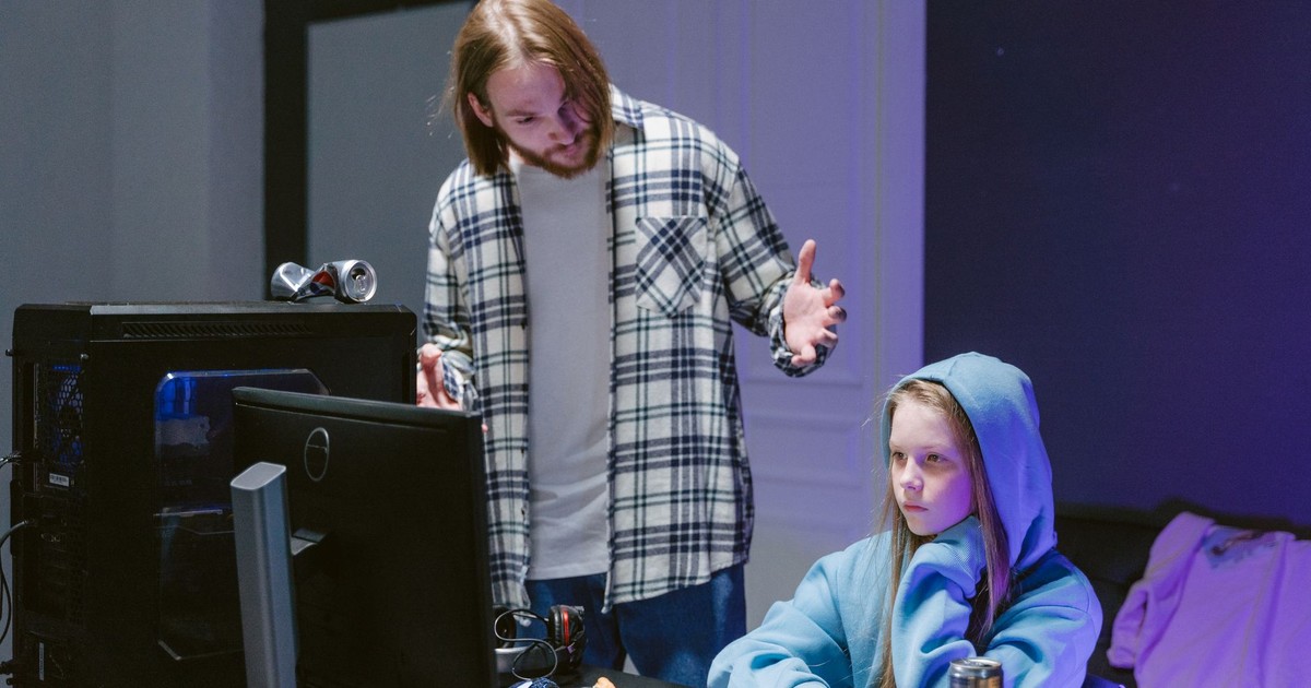 A father scolds his daughter playing video games on a computer, creating a tense moment.