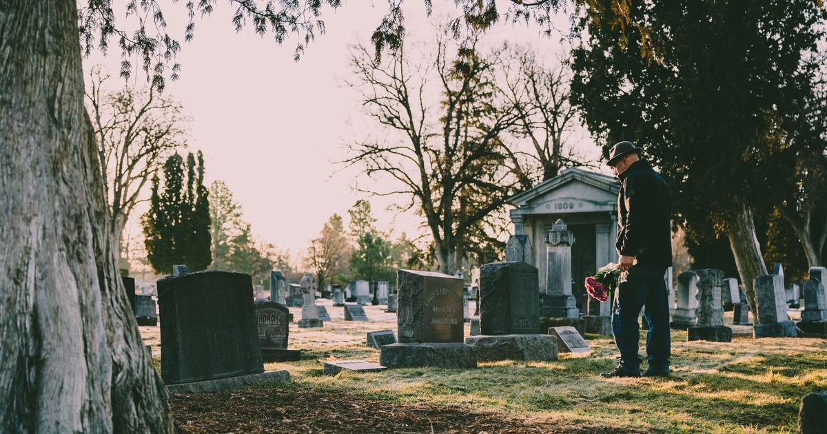 A person stands in a peaceful cemetery holding flowers in remembrance.