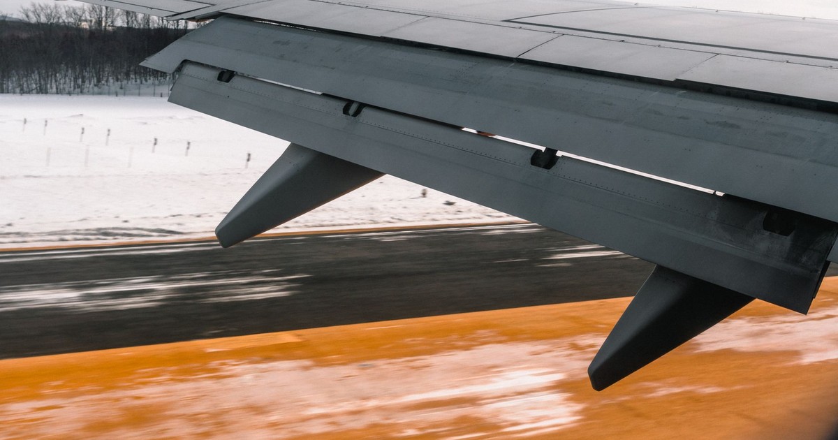 Close-up of an airplane wing during landing on a snowy runway, showcasing aviation dynamics.