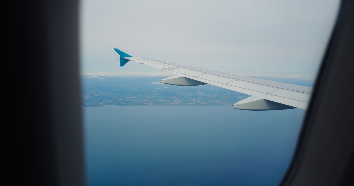 Scenic aerial view from an airplane window showing ocean and distant land below a clear sky.