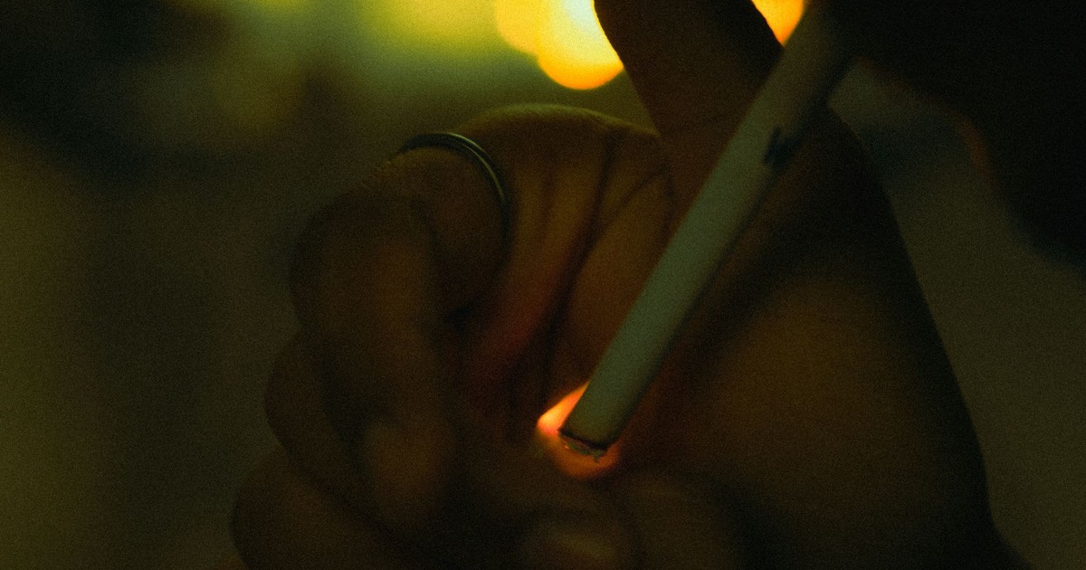 Atmospheric close-up of a hand lighting a cigarette, captured in low light.