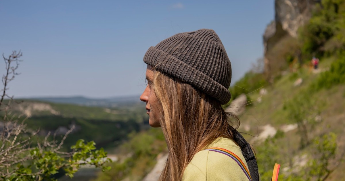 A woman wearing a hat enjoys the scenic mountain landscape during a sunny hike.