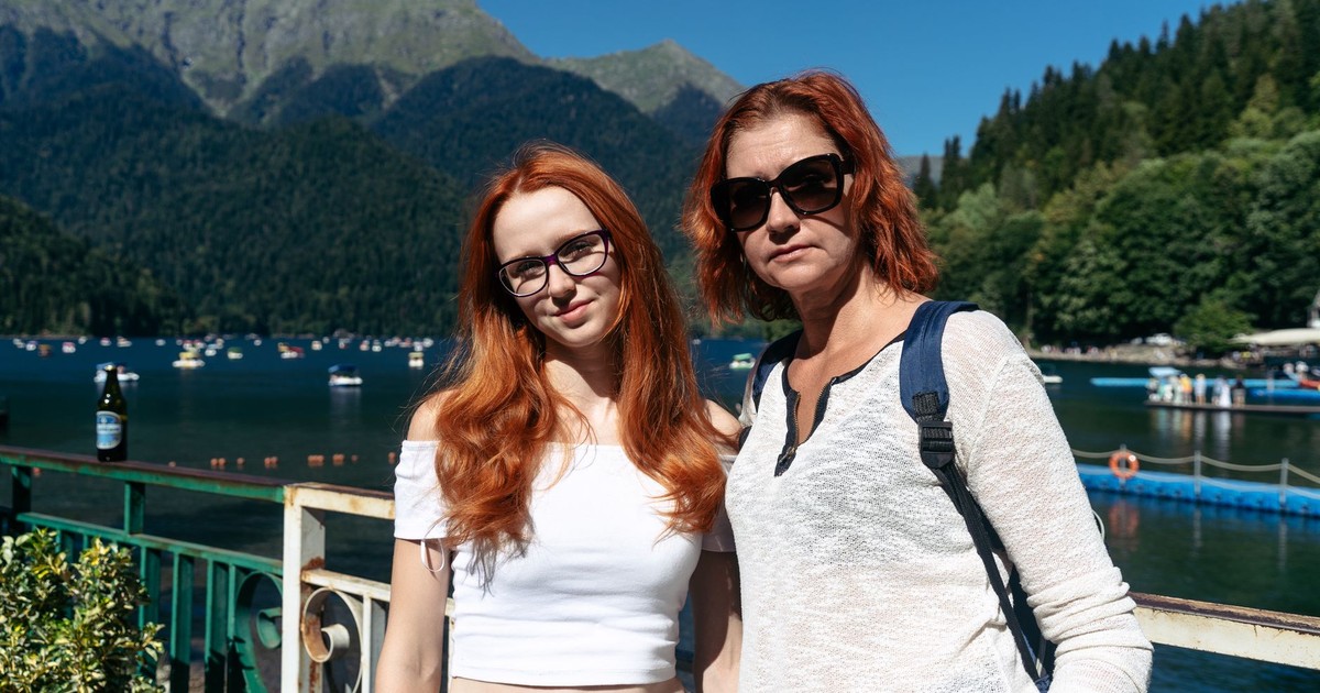 Two women enjoying a sunny day by a lake with mountains in the background.